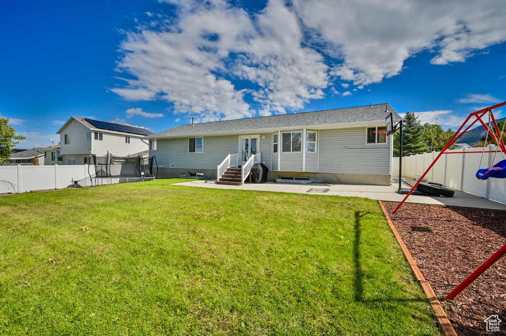 Back of property featuring a trampoline, fence, a yard, and a patio area
