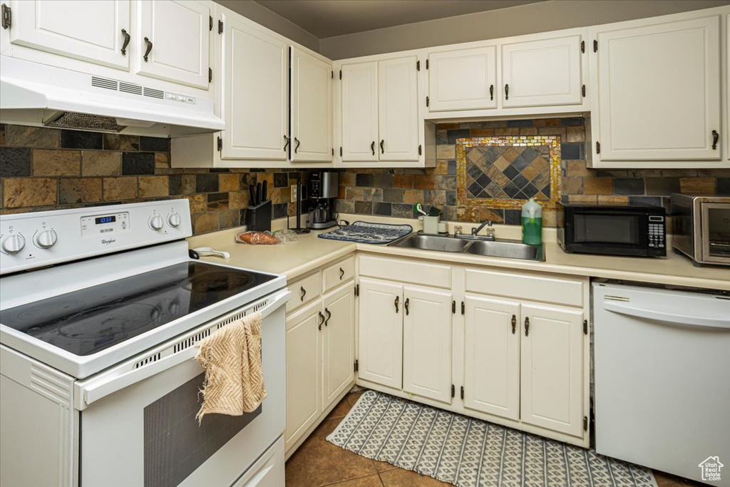 Kitchen with a sink, light countertops, under cabinet range hood, white appliances, and backsplash