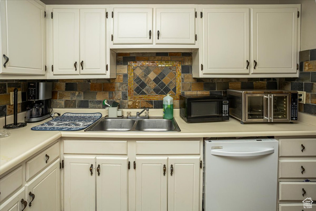 Kitchen with black microwave, white cabinets, white dishwasher, and a sink