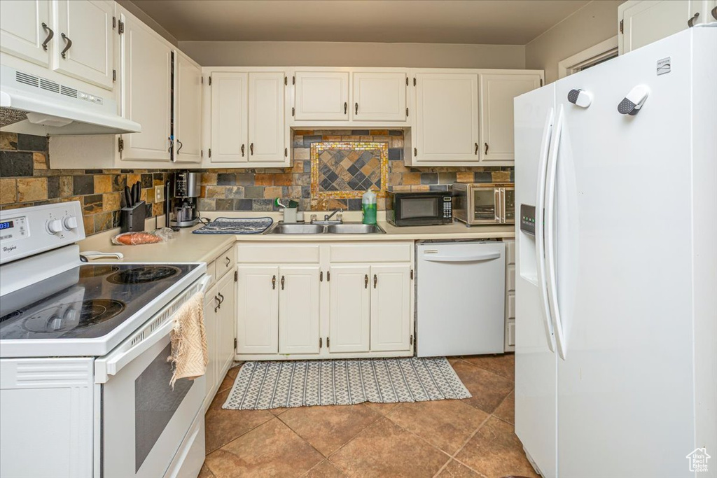 Kitchen with a sink, light countertops, under cabinet range hood, white appliances, and backsplash