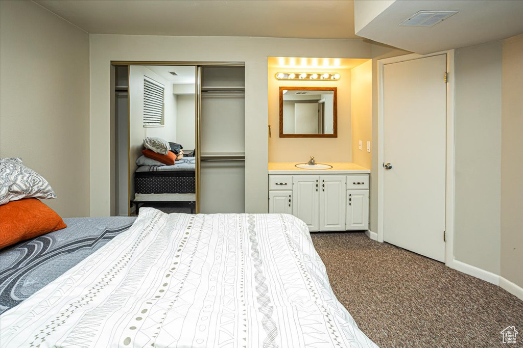 Bedroom with a closet, a sink, baseboards, visible vents, and dark carpet