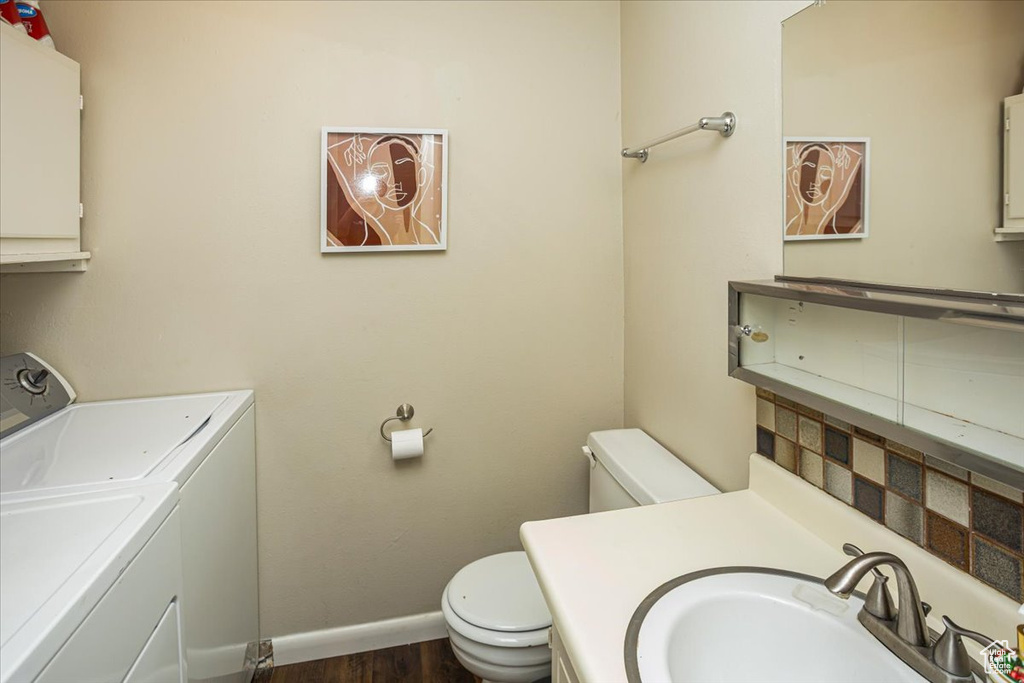 Bathroom featuring vanity, washing machine and dryer, toilet, baseboards, and wood finished floors