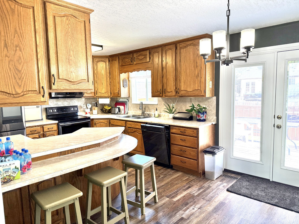 Kitchen with black appliances, a sink, light countertops, wood finished floors, and tasteful backsplash