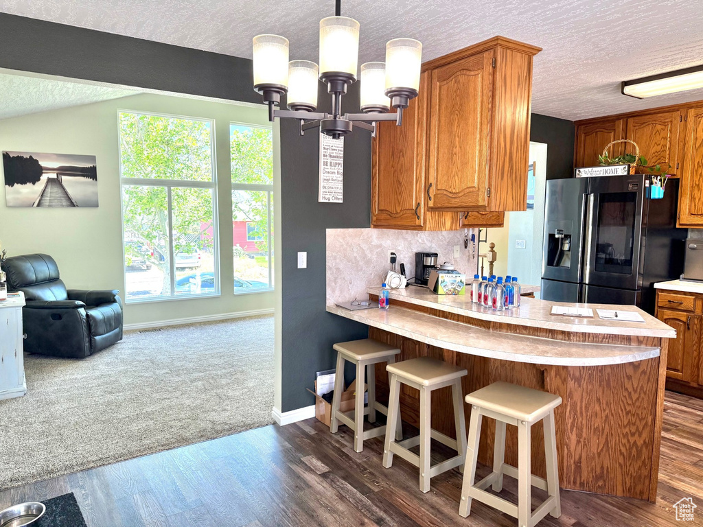 Kitchen featuring stainless steel refrigerator with ice dispenser, a textured ceiling, light countertops, and brown cabinetry