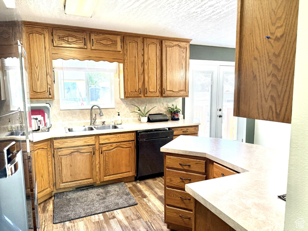Kitchen featuring black dishwasher, a sink, light wood-type flooring, light countertops, and decorative backsplash