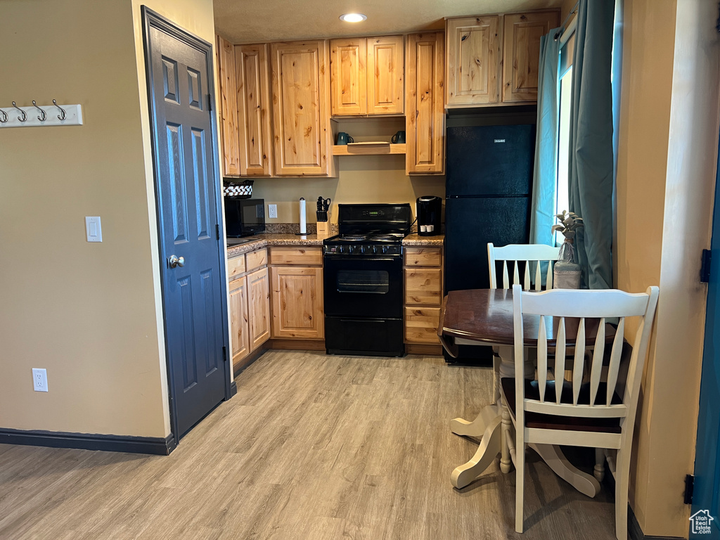 Kitchen with light brown cabinetry, baseboards, black appliances, and light wood-style floors