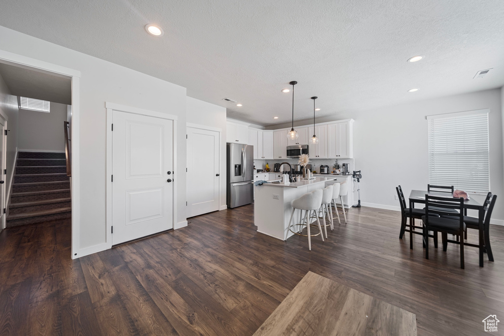 Kitchen featuring a sink, a breakfast bar, stainless steel appliances, visible vents, and a center island with sink