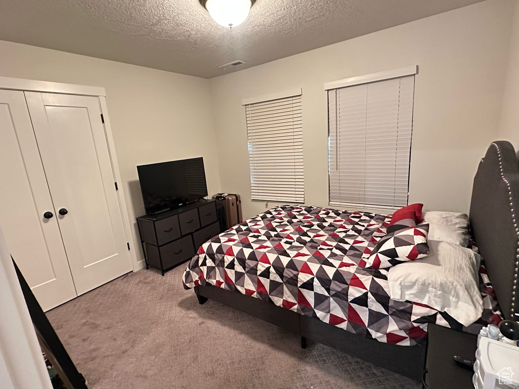 Carpeted bedroom with a textured ceiling, a closet, and visible vents