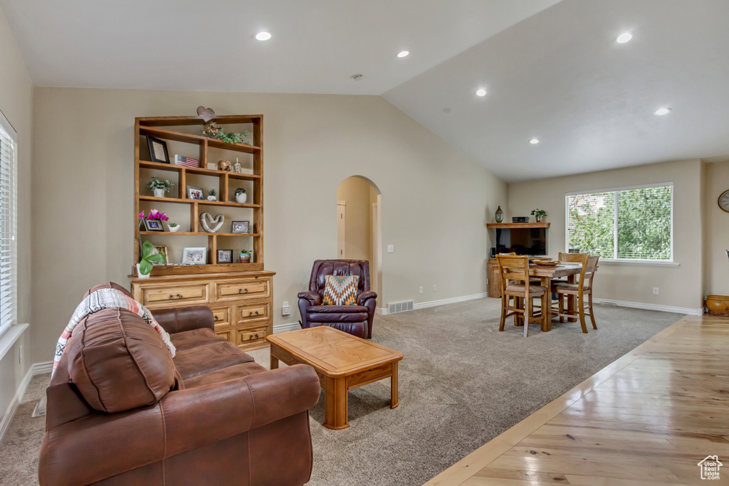Living room featuring visible vents, baseboards, arched walkways, hardwood / wood-style floors, and lofted ceiling