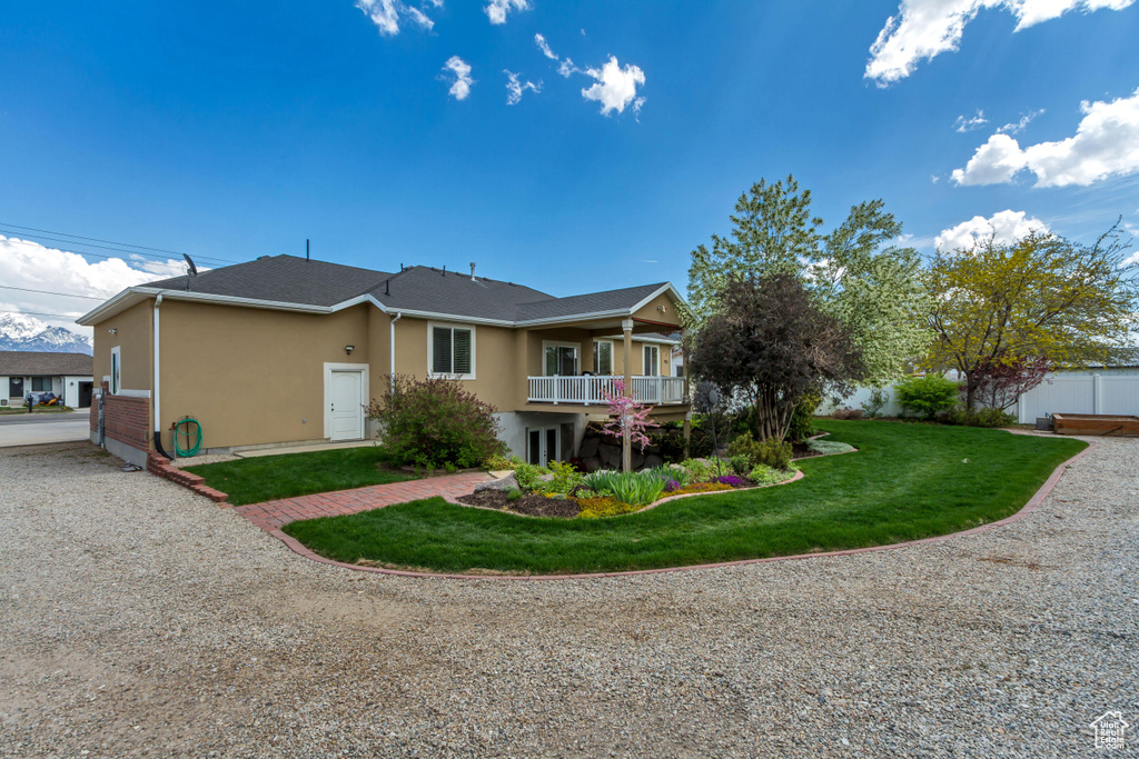Rear view of house with fence, stucco siding, a balcony, and a lawn