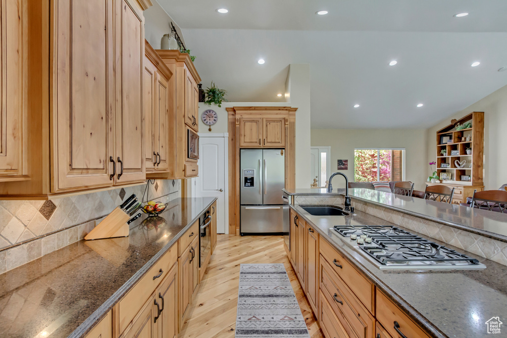 Kitchen featuring a sink, light wood-style floors, dark stone countertops, light brown cabinetry, and appliances with stainless steel finishes