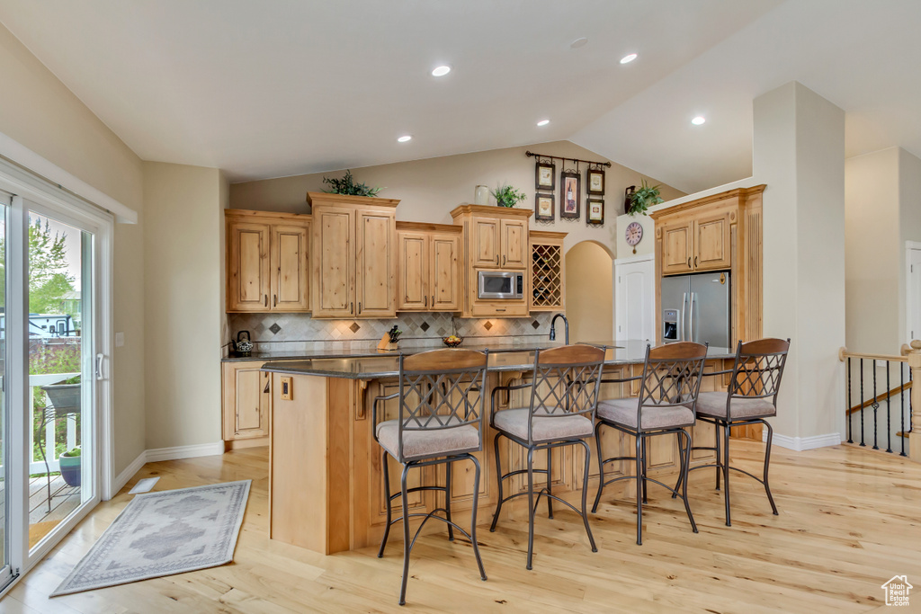 Kitchen featuring a kitchen bar, a spacious island, light wood-style flooring, dark countertops, and appliances with stainless steel finishes