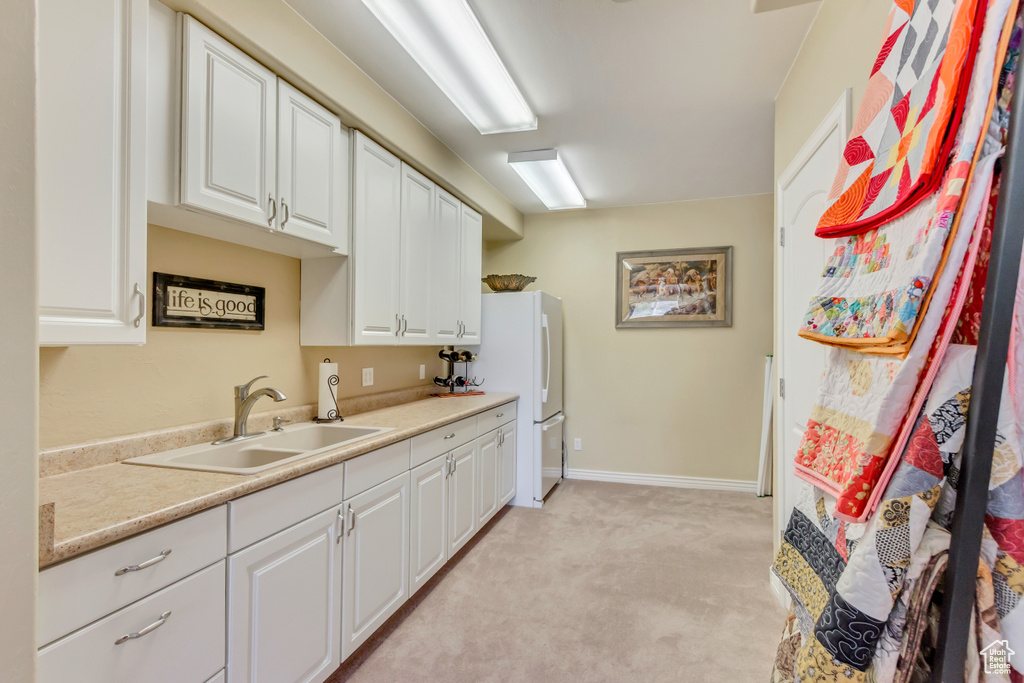 Kitchen with a sink, white cabinetry, light countertops, freestanding refrigerator, and light colored carpet