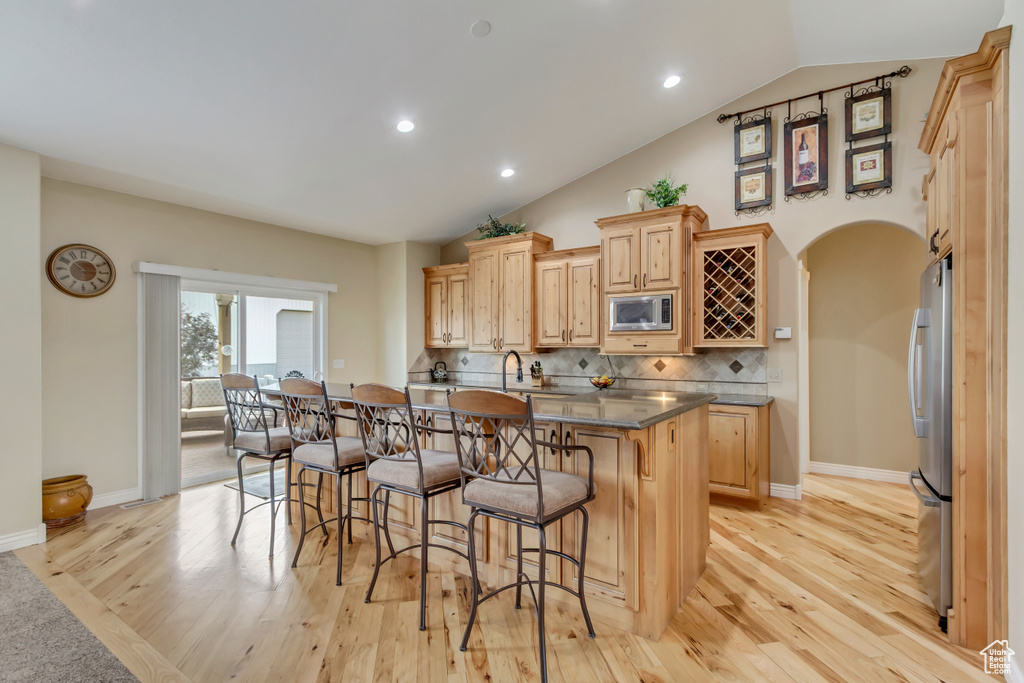 Kitchen featuring tasteful backsplash, light wood-type flooring, a breakfast bar, light brown cabinetry, and appliances with stainless steel finishes