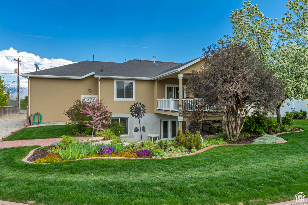 Back of house featuring stucco siding, a lawn, a balcony, and a shingled roof