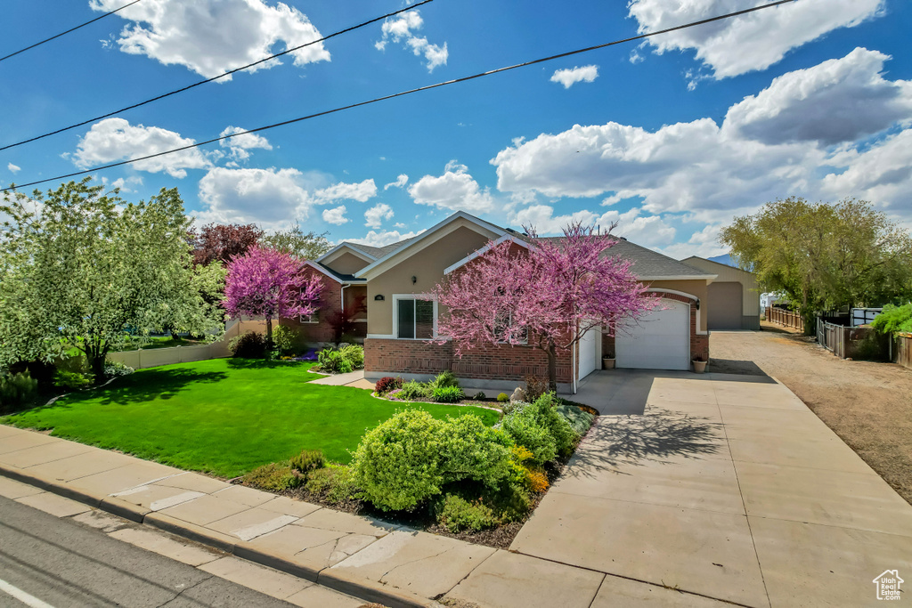 View of front facade featuring concrete driveway, stucco siding, fence, a front lawn, and a garage