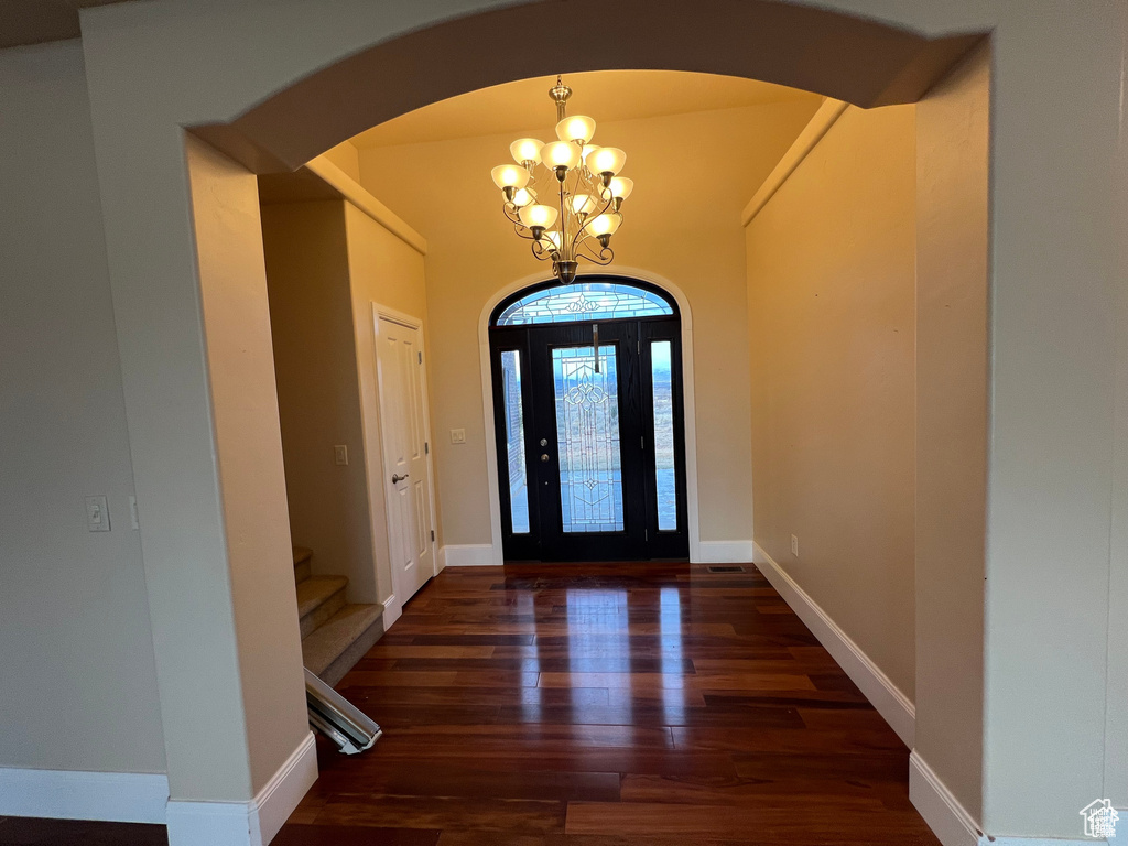 Foyer entrance featuring arched walkways, an inviting chandelier, stairs, and wood finished floors