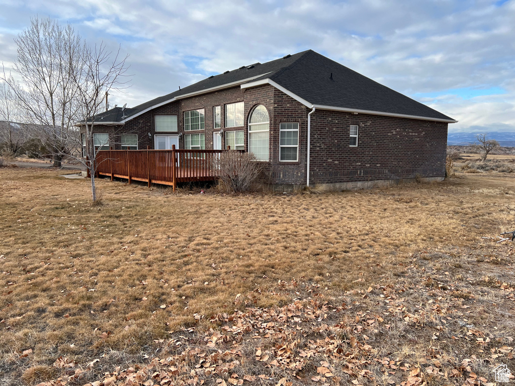 View of property exterior with a deck, a shingled roof, and brick siding