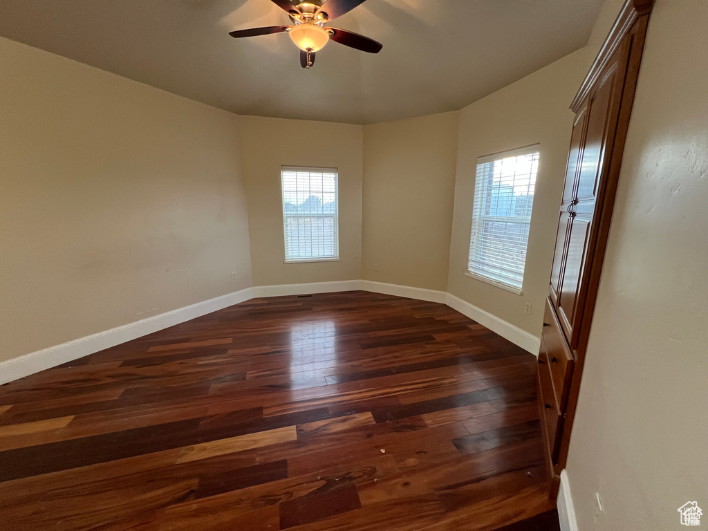 Spare room featuring baseboards, ceiling fan, a wealth of natural light, and dark wood-type flooring