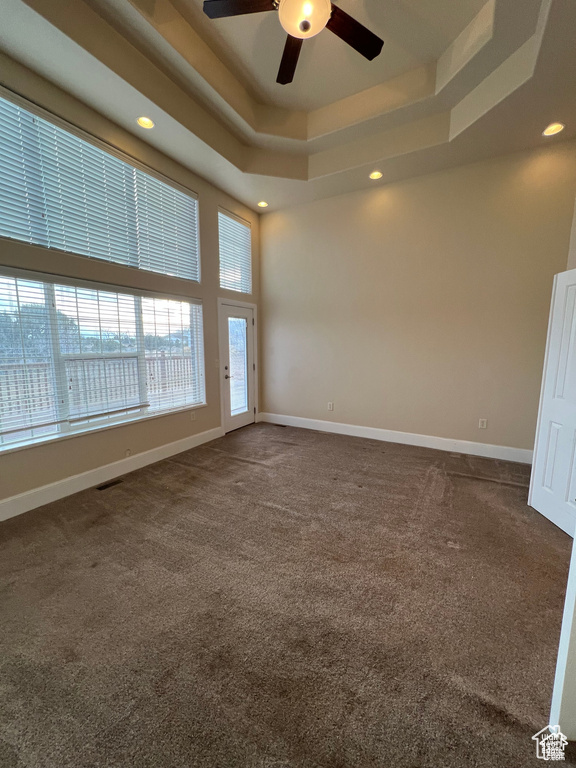 Empty room featuring dark colored carpet, a raised ceiling, baseboards, recessed lighting, and a ceiling fan