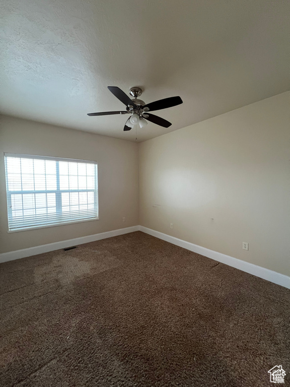 Empty room featuring a ceiling fan, visible vents, dark colored carpet, and baseboards