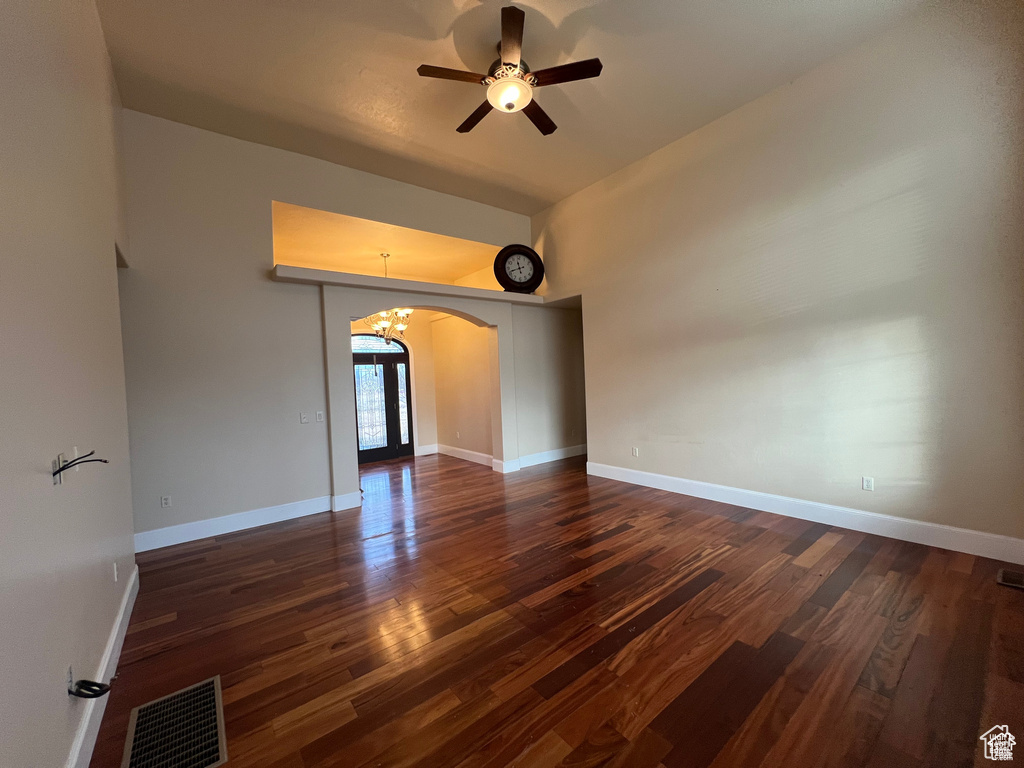 Empty room featuring dark wood finished floors, visible vents, arched walkways, and ceiling fan with notable chandelier