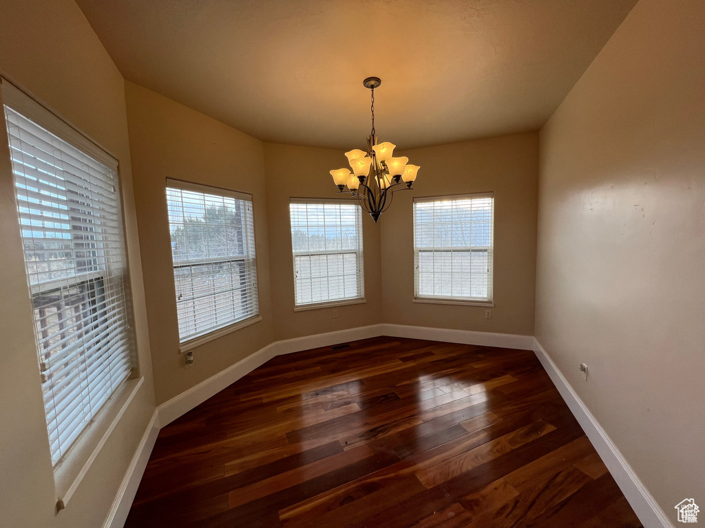Empty room with dark wood-style floors, baseboards, a chandelier, and a wealth of natural light
