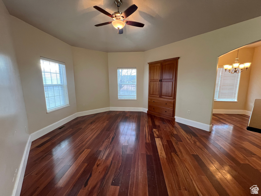 Unfurnished room with dark wood-style floors, ceiling fan with notable chandelier, baseboards, and plenty of natural light