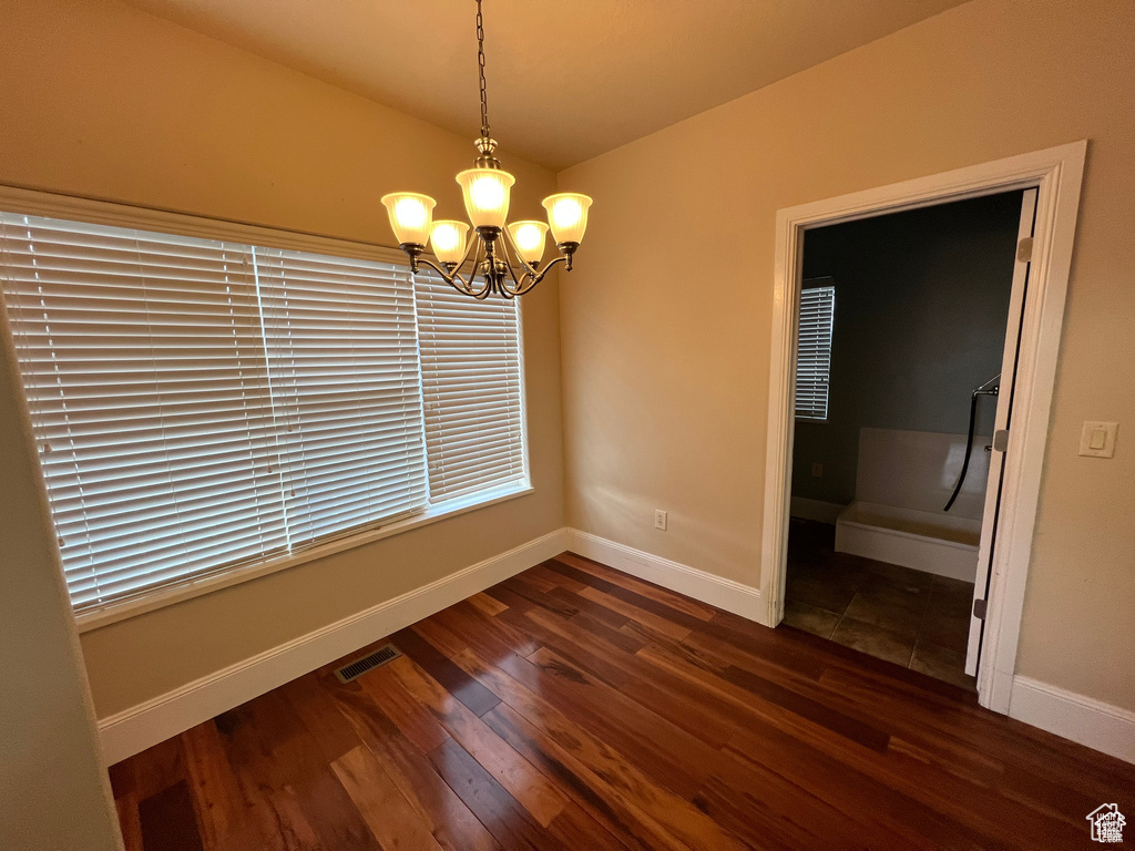 Unfurnished dining area with dark wood-style floors, an inviting chandelier, visible vents, and baseboards