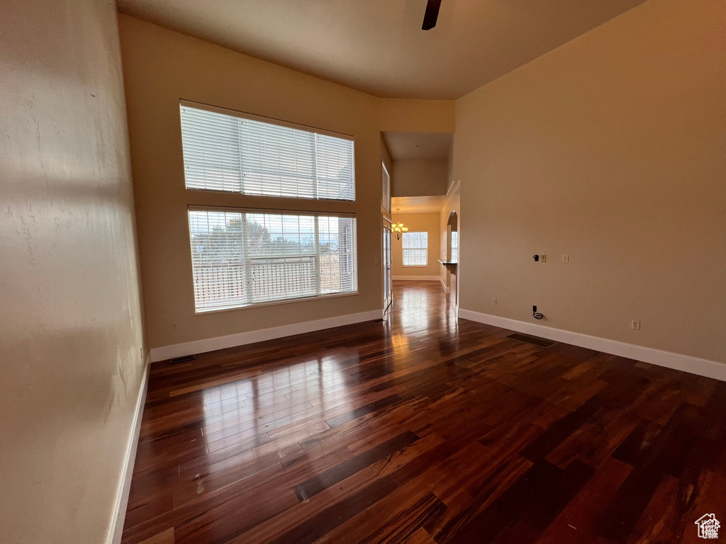 Spare room with dark wood-style flooring, baseboards, and ceiling fan with notable chandelier