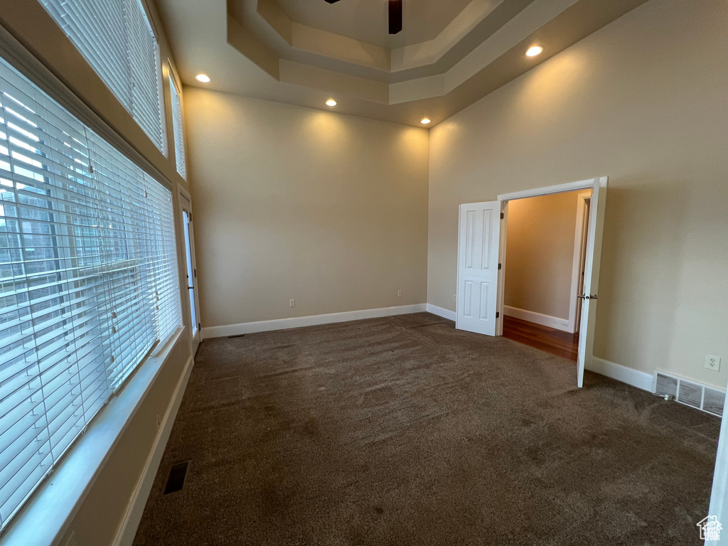 Unfurnished room with a high ceiling, visible vents, dark colored carpet, and plenty of natural light
