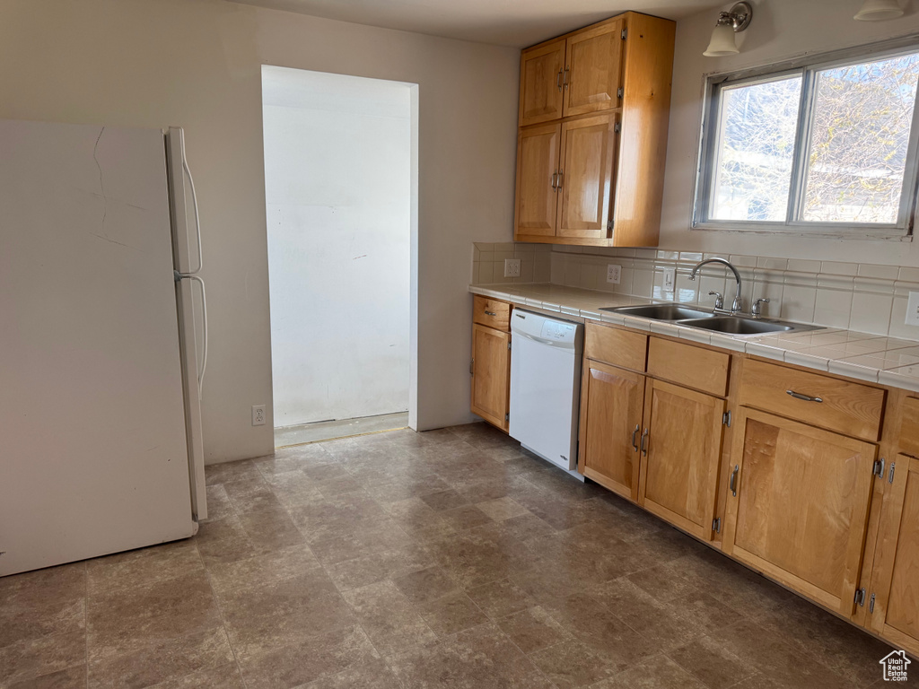 Kitchen featuring brown cabinets, tile countertops, a sink, white appliances, and tasteful backsplash