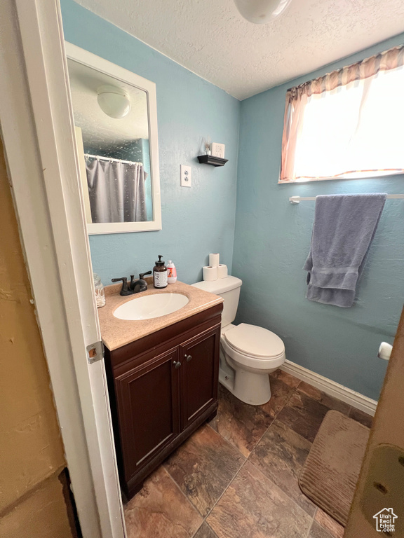 Full bath with toilet, a textured ceiling, stone finish floor, and vanity
