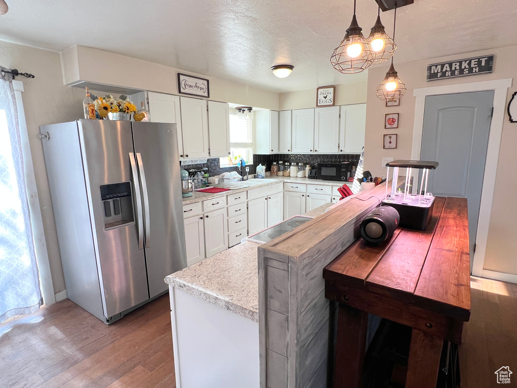 Kitchen with stainless steel fridge, black microwave, light countertops, white cabinets, and wood finished floors