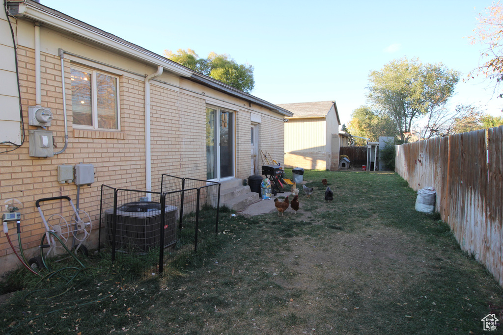 Rear view of house with central AC, entry steps, brick siding, and a fenced backyard