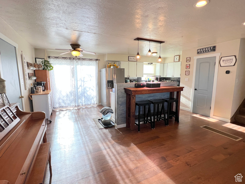 Kitchen with ceiling fan, decorative light fixtures, a textured ceiling, white cabinets, and wood finished floors