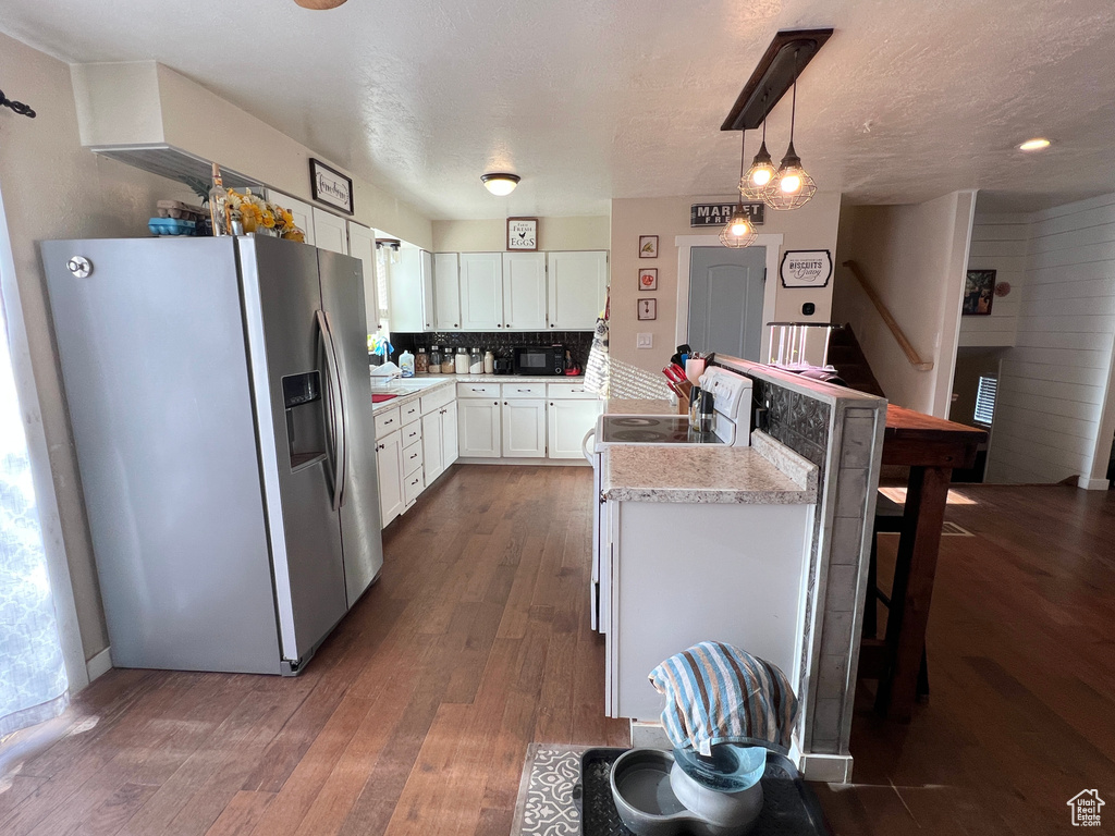 Kitchen with dark wood-style floors, stainless steel refrigerator with ice dispenser, white cabinetry, a peninsula, and light countertops
