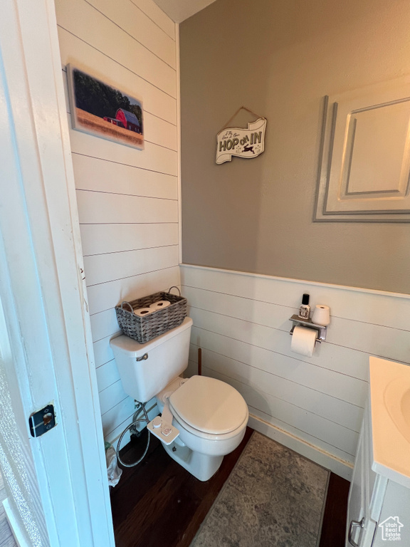 Half bath with wood walls, vanity, toilet, and wainscoting