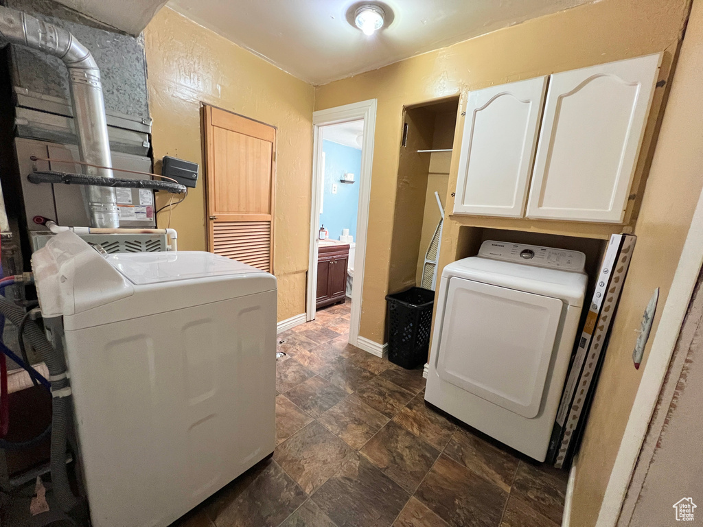 Laundry room featuring washing machine and dryer, cabinet space, stone finish floor, and baseboards