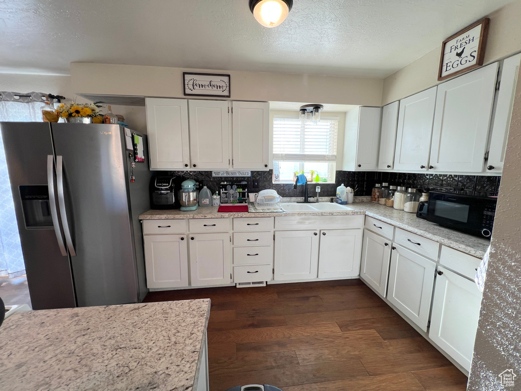 Kitchen featuring a sink, dark wood-style flooring, black microwave, stainless steel refrigerator with ice dispenser, and white cabinets