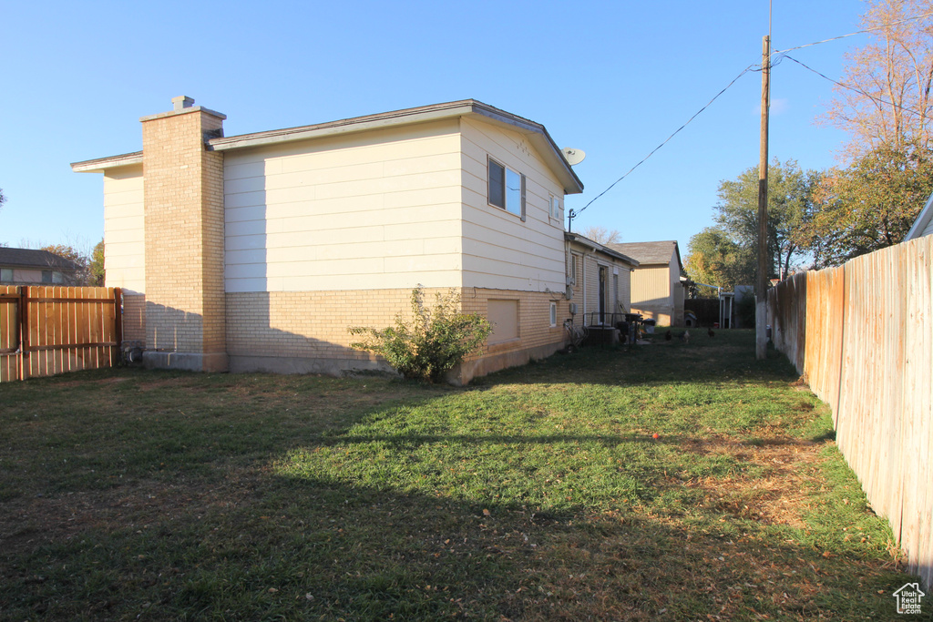 View of side of property with a chimney, brick siding, a fenced backyard, and a yard