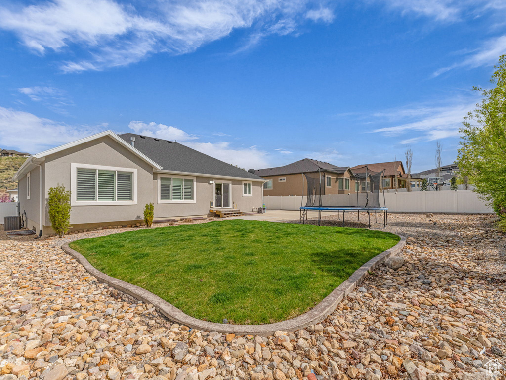 Back of property with a patio, a trampoline, stucco siding, a yard, and a fenced backyard