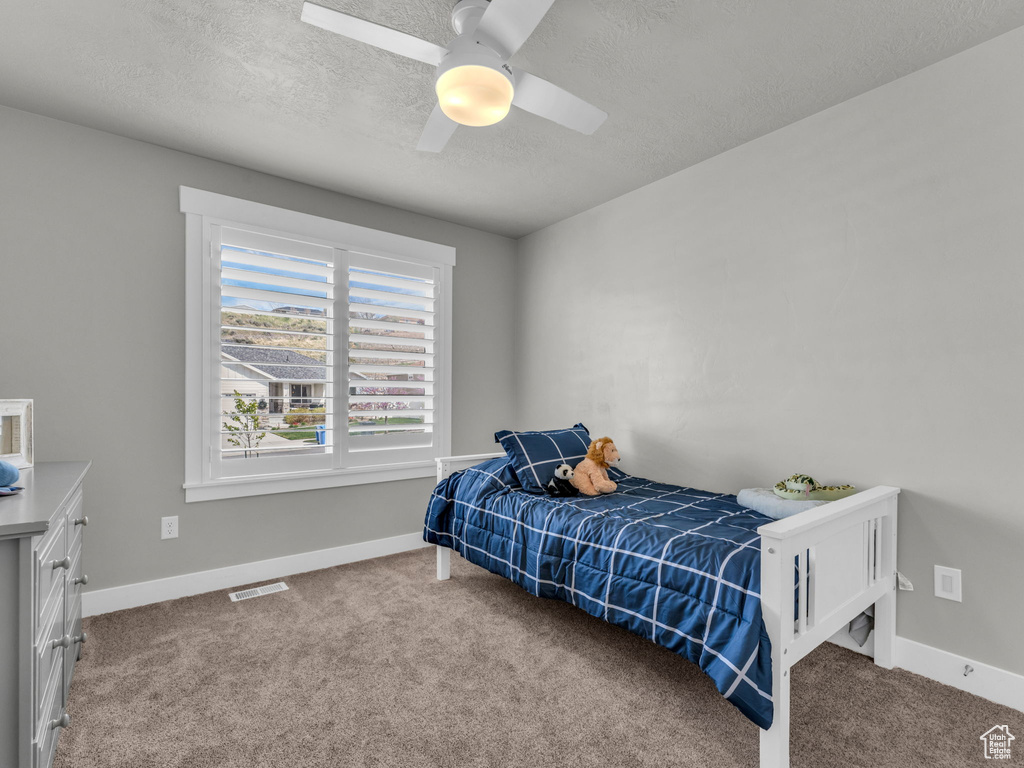 Carpeted bedroom featuring a textured ceiling, visible vents, ceiling fan, and baseboards