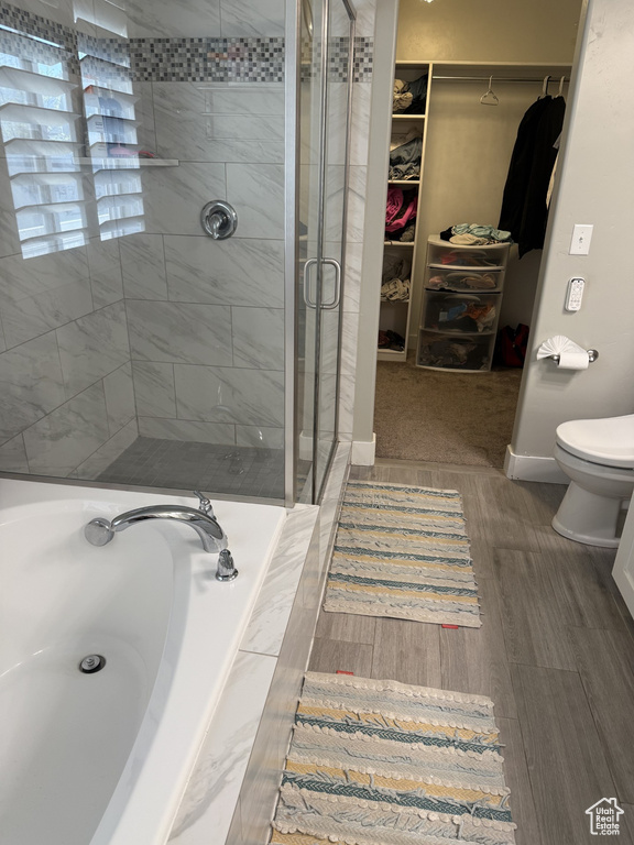 Bathroom featuring a shower stall, a garden tub, toilet, a walk in closet, and wood finished floors
