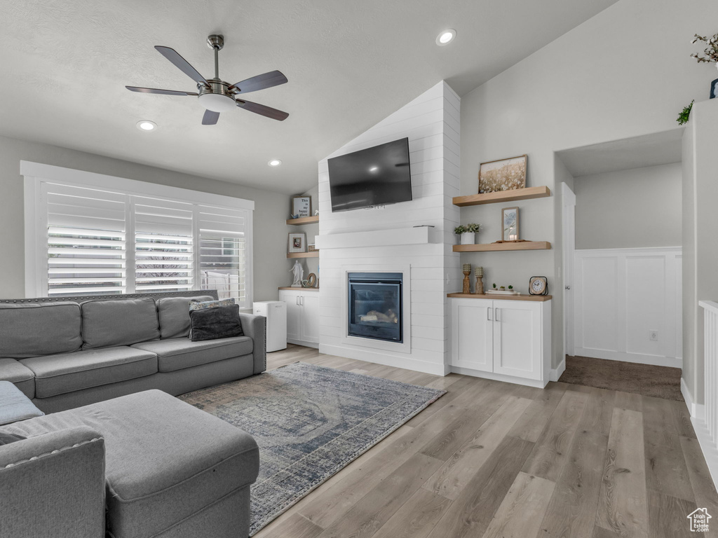 Living area featuring a large fireplace, ceiling fan, a wainscoted wall, light wood-style flooring, and lofted ceiling