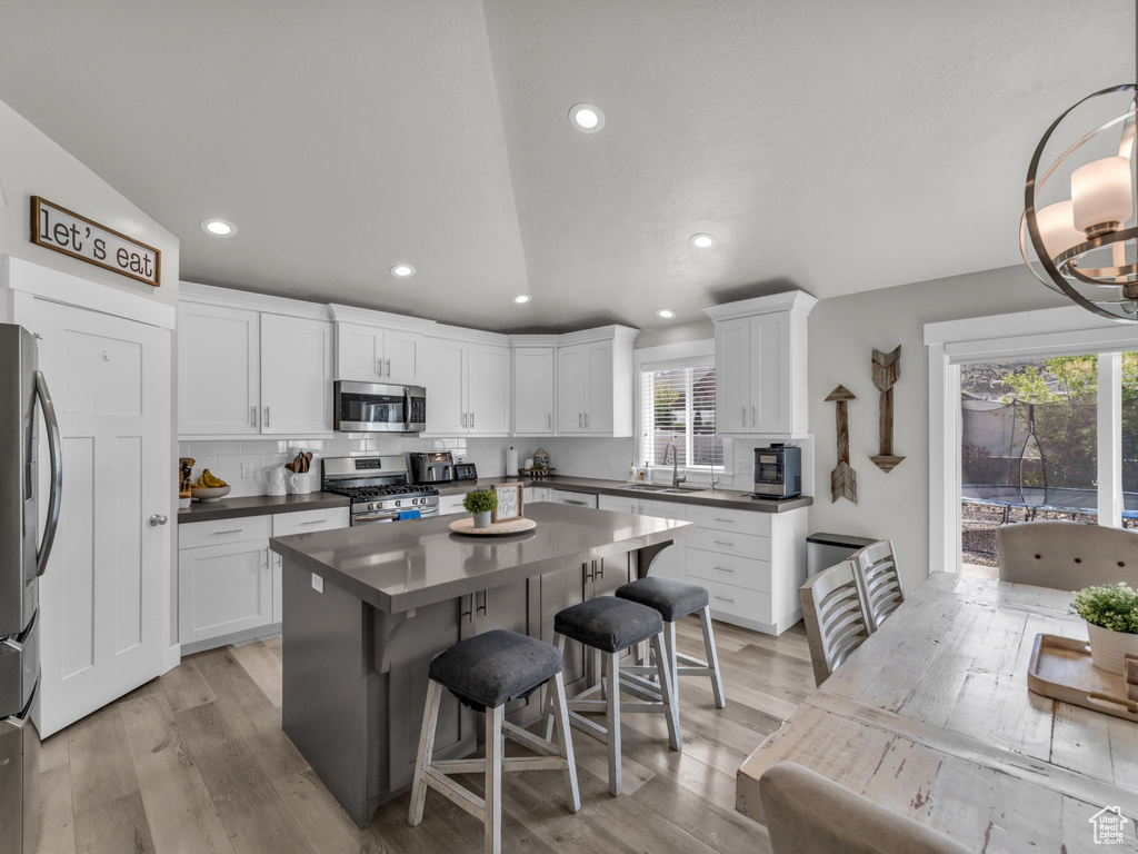 Kitchen featuring recessed lighting, a sink, a kitchen bar, dark countertops, and appliances with stainless steel finishes