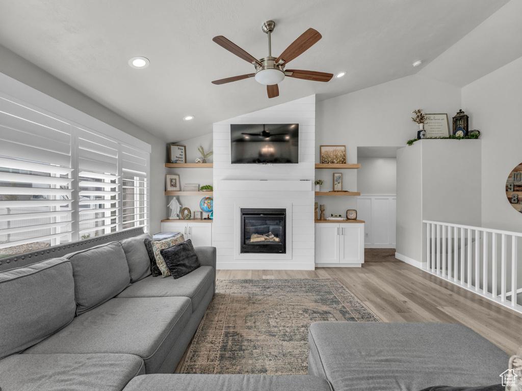 Living room featuring recessed lighting, vaulted ceiling, ceiling fan, a fireplace, and light wood-type flooring