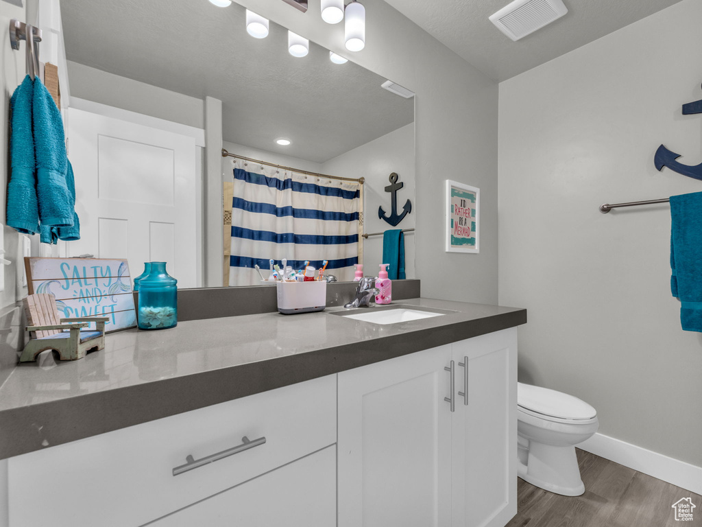 Bathroom with vanity, toilet, visible vents, baseboards, and wood finished floors