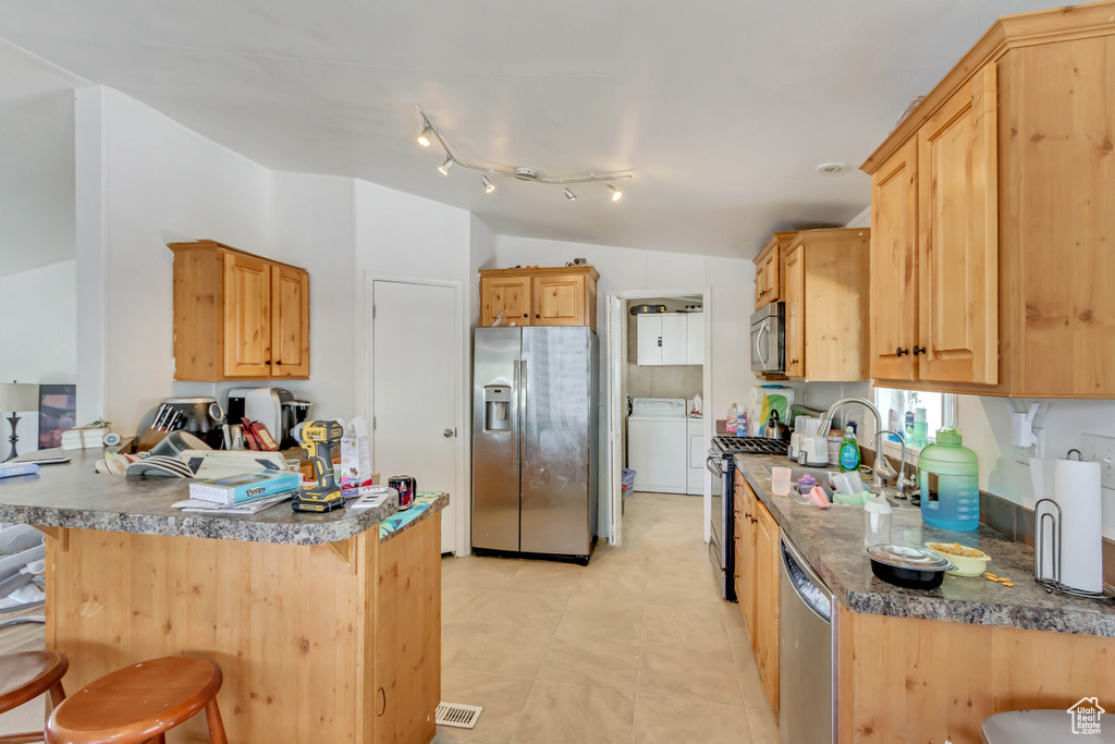 Kitchen with lofted ceiling, a kitchen breakfast bar, washer / clothes dryer, stainless steel appliances, and a peninsula