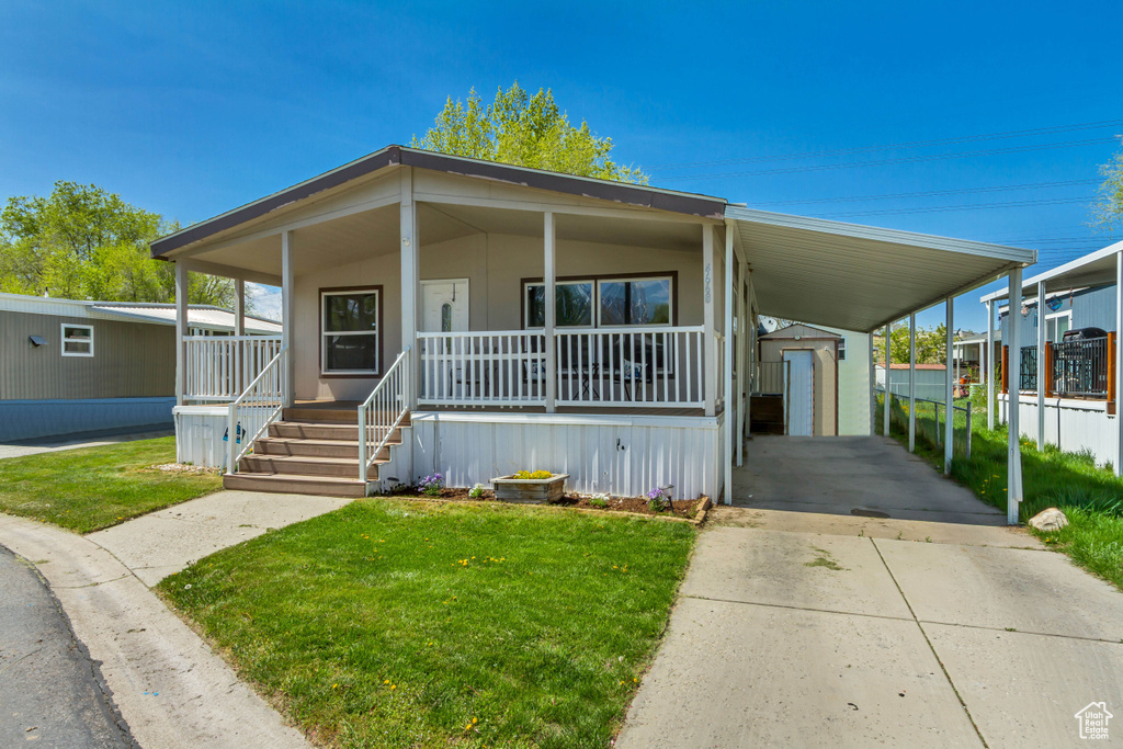 Manufactured / mobile home with driveway, covered porch, an attached carport, and a front lawn